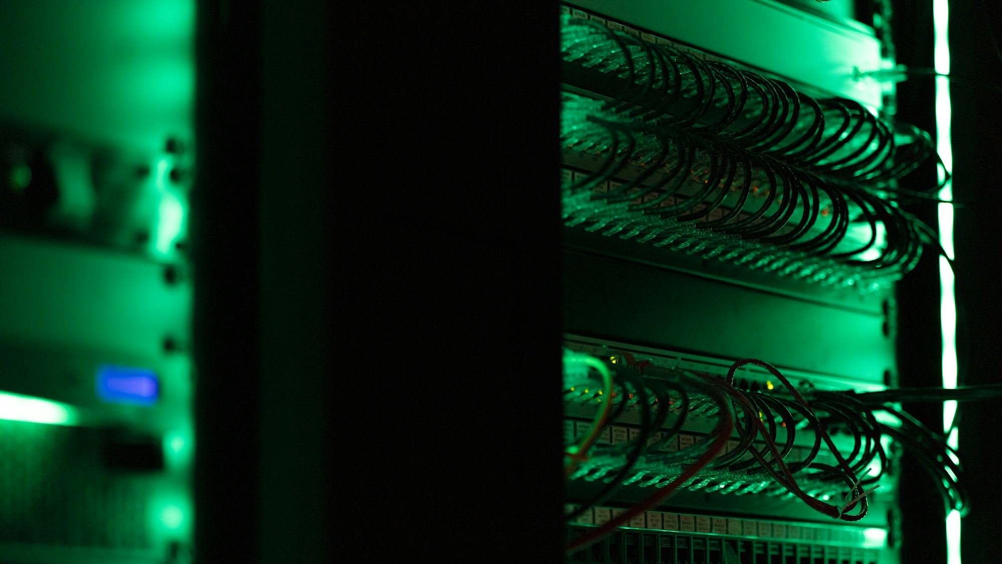 Network cables in a dark equipment rack lit by green status lights